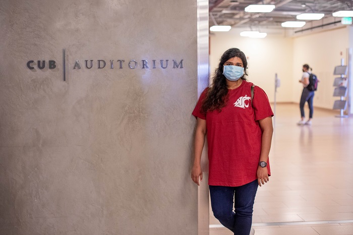 Girl wearing a mask and standing next to CUB Auditorium