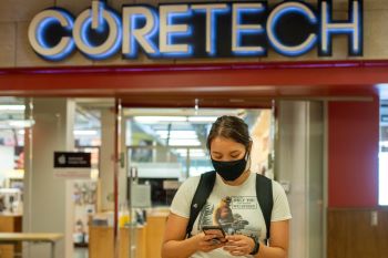 Girl using phone and wearing a mask in front of the CORETECH store