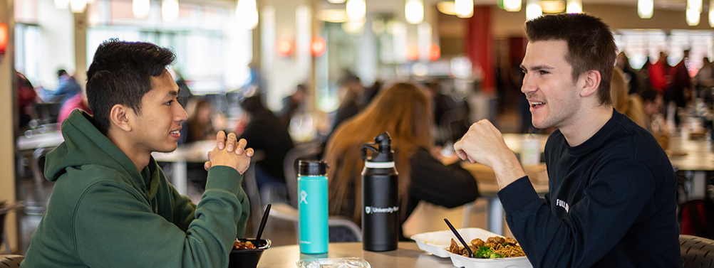 Two students talk seated at table